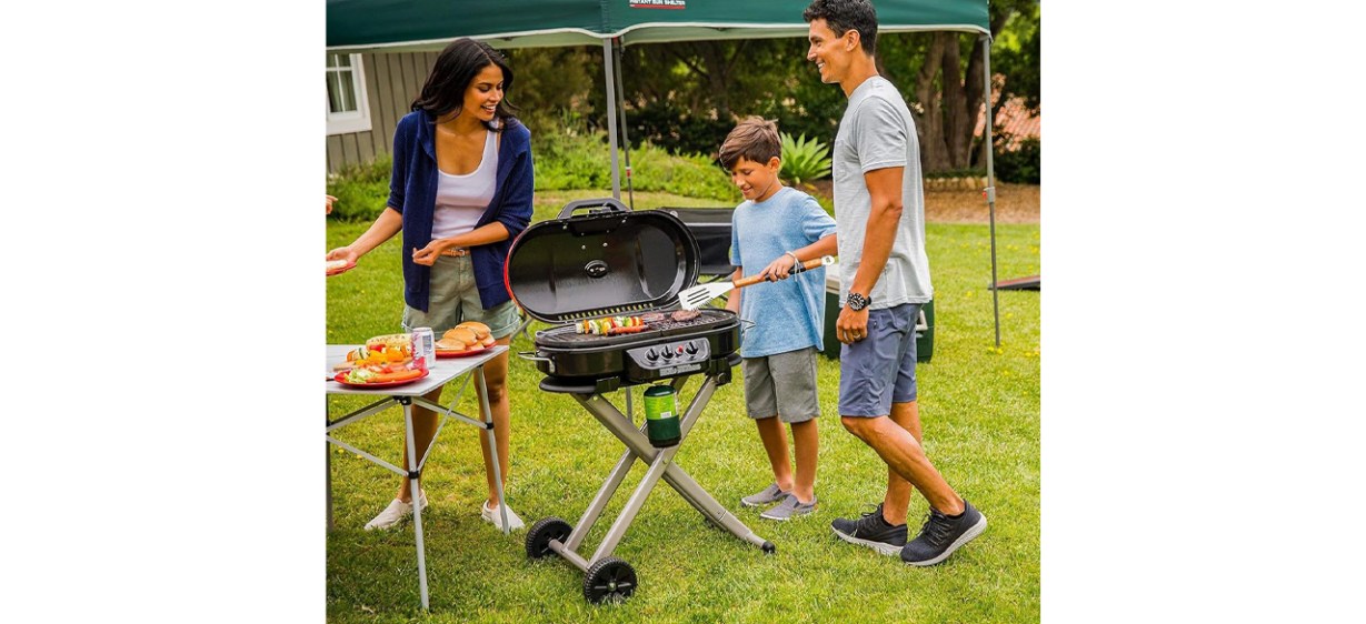 Family grilling on lawn with Coleman RoadTrip 285 Portable Stand-Up Propane Grill