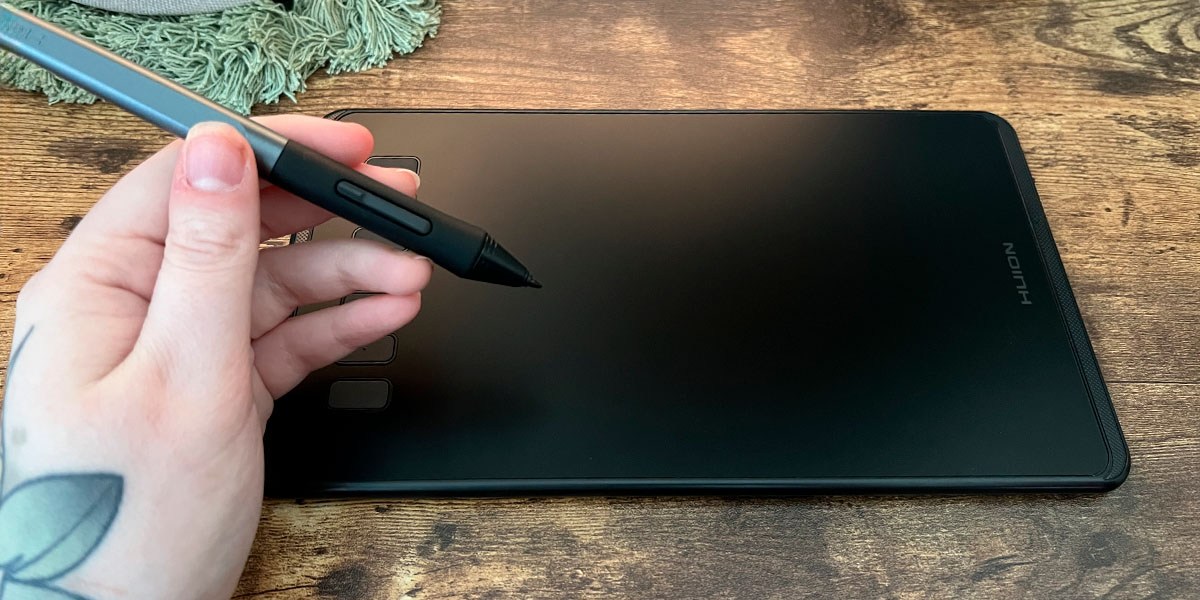 Hand holding pen in front of HUION  Inspiroy H640P