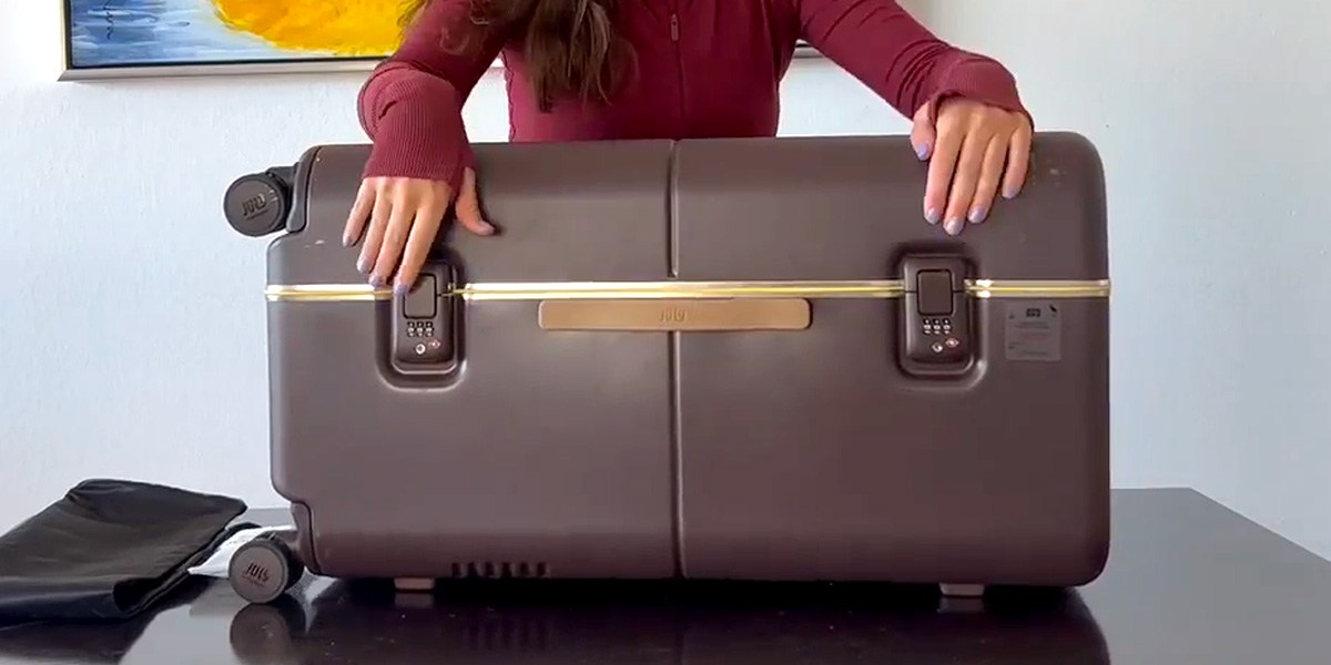 Closed July Checked Trunk on table with person's hands on locks Closed July Checked Trunk on table with person's hands on locks